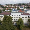 Das Gebäude des Landratsamtes ist aus der Luft zu sehen. Im Hintergrund stehen weitere Häuser. Vor dem Landratsamt sind große Bäume.