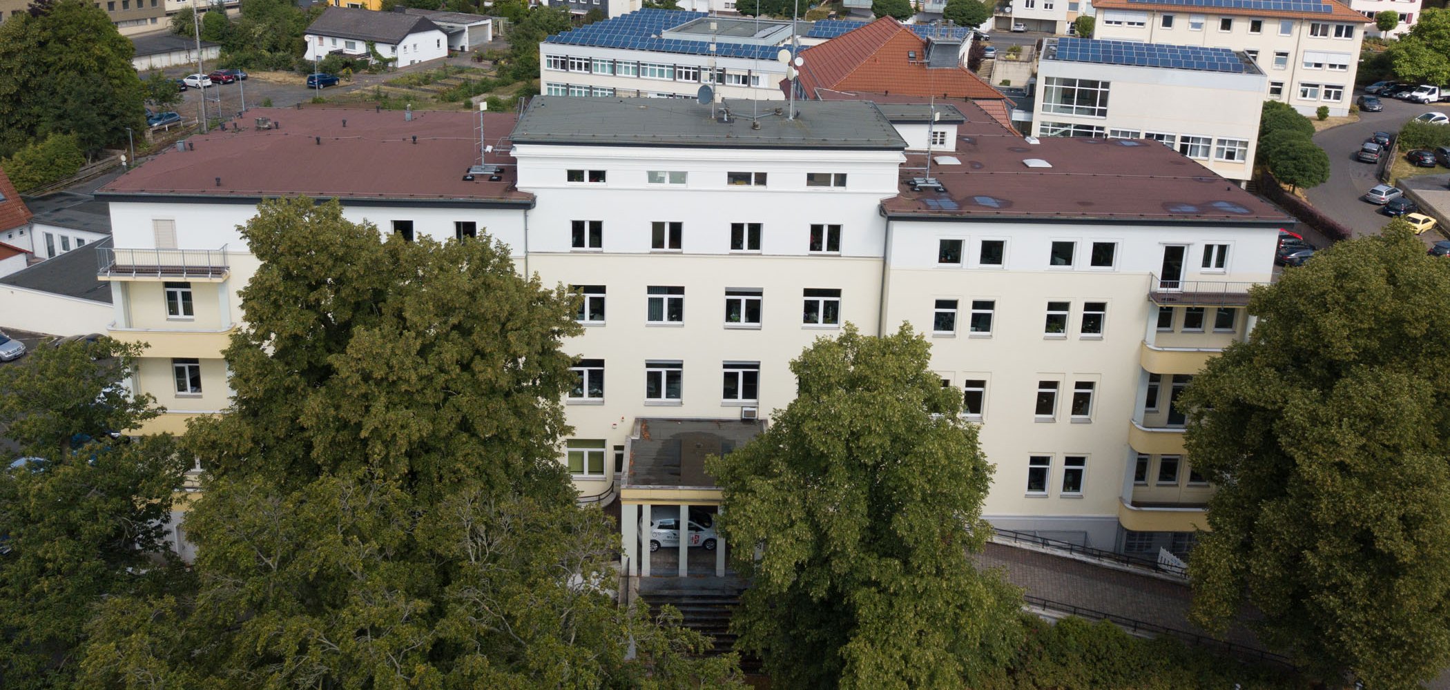 Das Gebäude des Landratsamtes ist aus der Luft zu sehen. Im Hintergrund stehen weitere Häuser. Vor dem Landratsamt sind große Bäume.