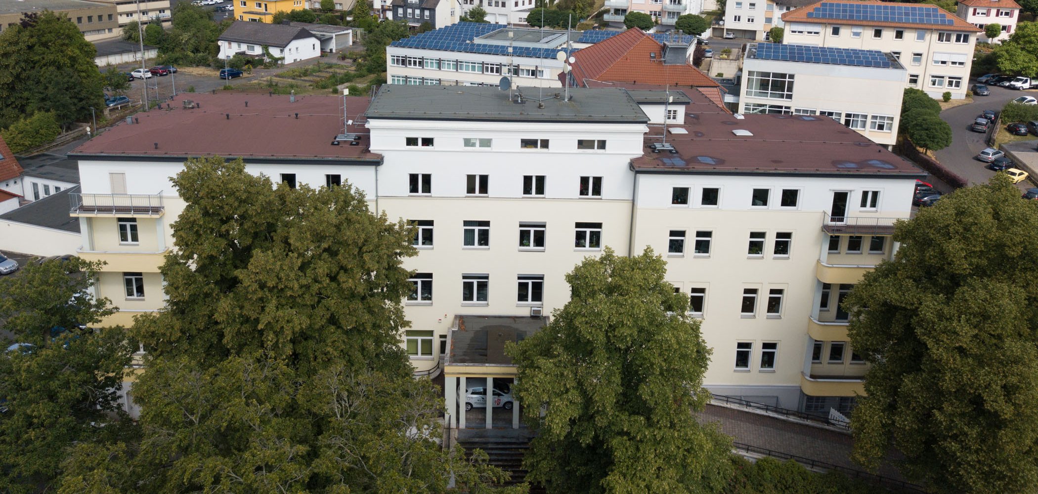 Das Gebäude des Landratsamtes ist aus der Luft zu sehen. Im Hintergrund stehen weitere Häuser. Vor dem Landratsamt sind große Bäume.