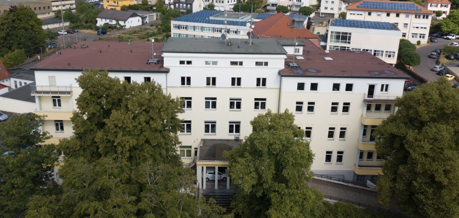 Das Gebäude des Landratsamtes ist aus der Luft zu sehen. Im Hintergrund stehen weitere Häuser. Vor dem Landratsamt sind große Bäume.