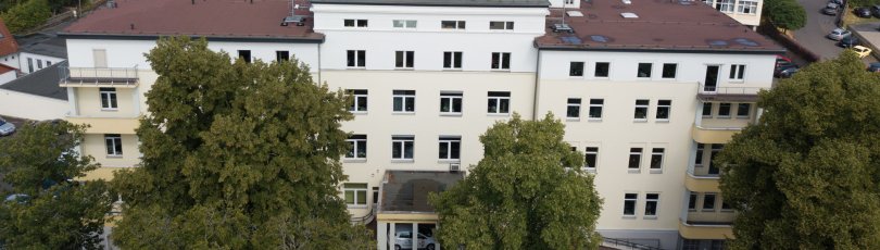 Das Gebäude des Landratsamtes ist aus der Luft zu sehen. Im Hintergrund stehen weitere Häuser. Vor dem Landratsamt sind große Bäume.