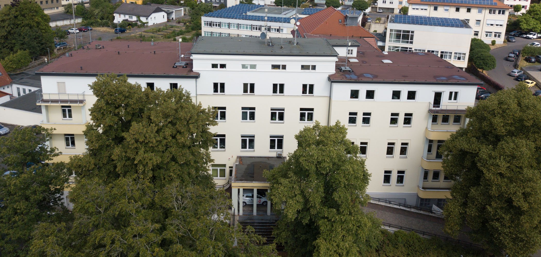 Das Gebäude des Landratsamtes ist aus der Luft zu sehen. Im Hintergrund stehen weitere Häuser. Vor dem Landratsamt sind große Bäume.