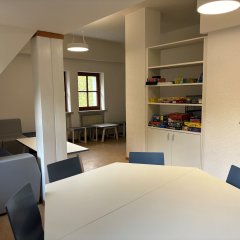 In einem Raum steht ein Tisch. In der hinteren Ecke siegt man eine Sitzecke mit einer Bank. Im Raum gibt es Brettspiele.