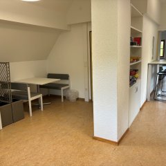 In einem leicht abgelegenen Teil eines Raumes stehen zwei Tische mit mehreren Sitzmöglichkeiten.