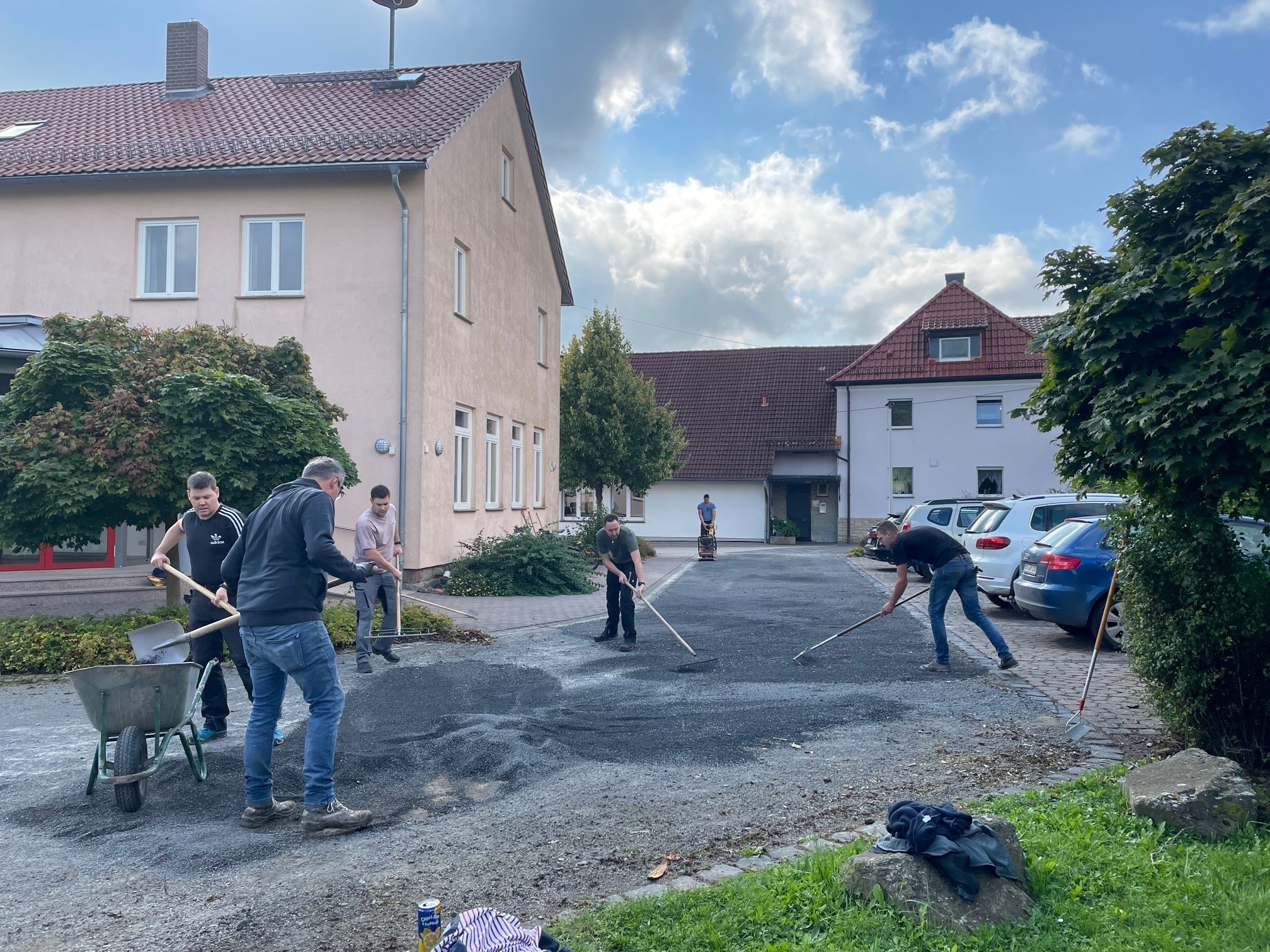 Mehrere Freiwillige helfen dabei eine Straße zu befestigen. Am Rand und im Hintergrund sieht man Häuser.