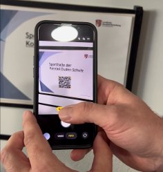 Eine Person scannt mit dem Smartphone einen QR-Code auf einem Aushang der Sporthalle der Konrad-Duden-Schule des Landkreises Hersfeld-Rotenburg.
