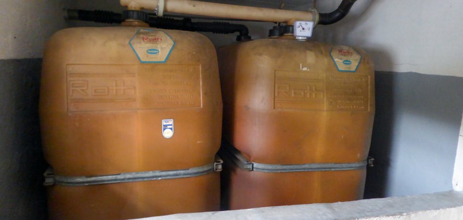 Nahaufnahme von zwei alten, orange-braunen Heizöltanks aus Polyethylen, die in einem Kellerraum stehen.