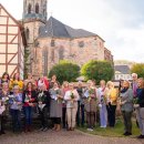 Eine Menschengruppe hauptsächlich aus geehrten Frauen, die jeweils eine Rose und Urkunde in der Hand halten, steht für ein Gruppenfoto vor einer Mauer in einem Garten. Im Hintergrund ist die Kirche von Rotenburg zu erkennen.