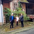 Landrat Torsten Warnecke (links) überreicht den Förderbescheid für den Beratungsvertrag an Alheims Bürgermeister Jochen Schmidt, zwischen den beiden steht SPD-Landtagsabgeordnete Karina Fissmann. Die drei stehen vor einer alten Fachwerkruine. 