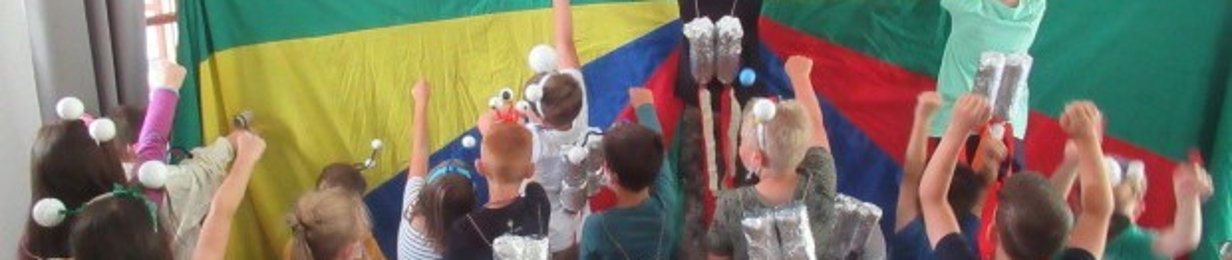 Rückansicht einer Kindergruppe, die alle eine silberne gebastelte Rakete auf ihren Rücken tragen. Die Kids strecken die Hände, als ob sie auf den Mars reisen. Sie stehen vor einer bunten Wand. 