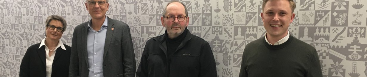 Der Jugendhilfeausschuss bestehend aus Anette Kranz (Leiterin Fachdienst Kinder- u. Jugendhilfe), Dirk Noll (Erster Kreisbeigeordneter), Ralf Bartholmai (Geschäftsführer der Drogenhilfe Nordhessen e.V.) und Julian Gilbert (Verwaltungsleiter des FB Jugend, Soziales und Senioren) stehen vor einer Wand mit Wappentapete.