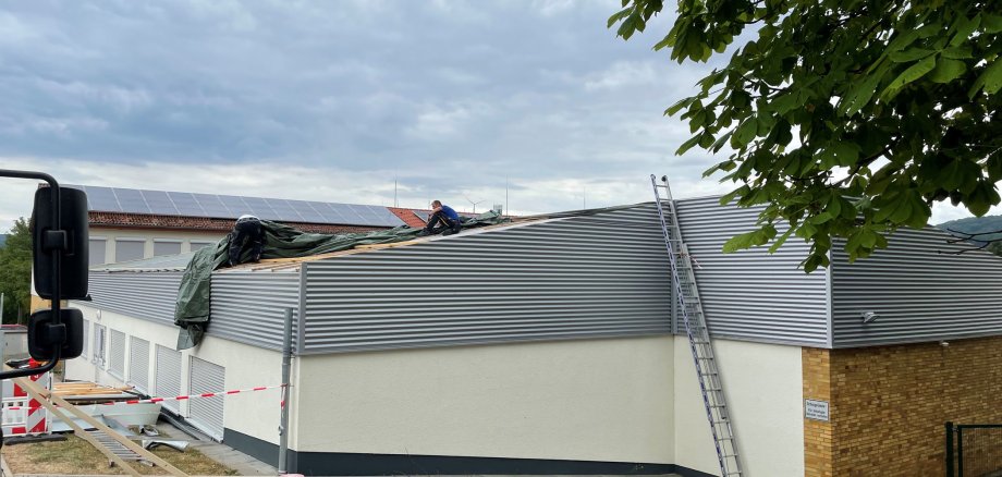 Das Dach einer Schule ist beschädigt. Ein Mann sitzt auf dem Dach und arbeitet daran. 