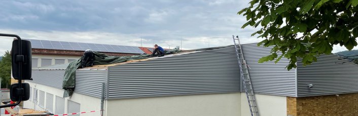 Das Dach einer Schule ist beschädigt. Ein Mann sitzt auf dem Dach und arbeitet daran. 