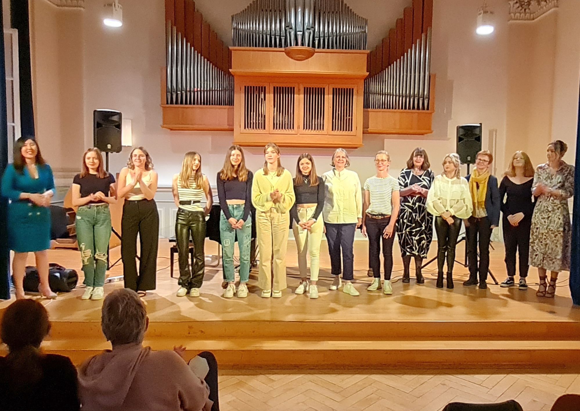 Schülerinnen der Musikschule stehen in einer Reihe auf der Bühne. Im Hintergrund an der Wand hängt eine Orgel.