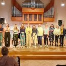 Schülerinnen der Musikschule stehen in einer Reihe auf der Bühne. Im Hintergrund an der Wand hängt eine Orgel. 