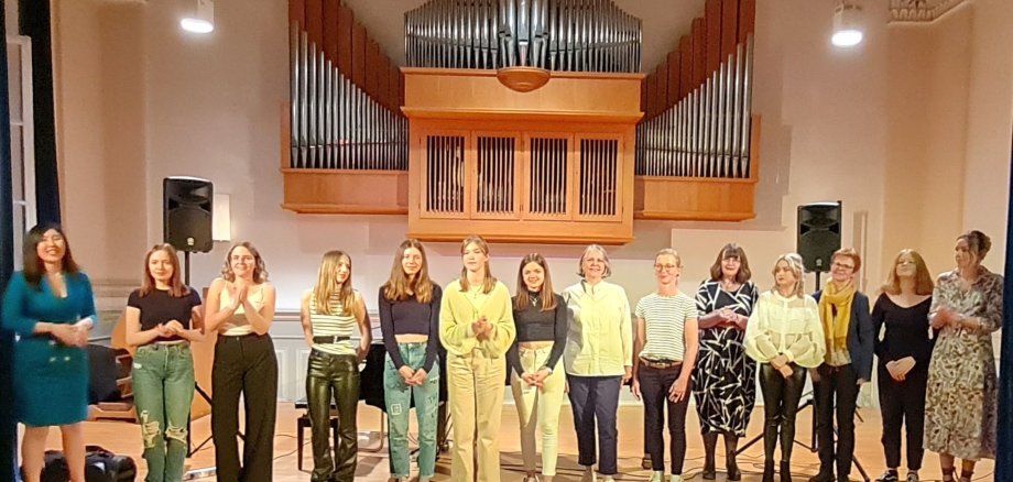 Schülerinnen der Musikschule stehen in einer Reihe auf der Bühne. Im Hintergrund an der Wand hängt eine Orgel. 