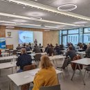 Mehrere Personen sitzen an Tischen im Kreistagssitzungssaal der Kreisverwaltung. An der Wand wird eine Präsentation gezeigt. Landrat Warnecke hält ein Mikrofon und erzählt etwas.