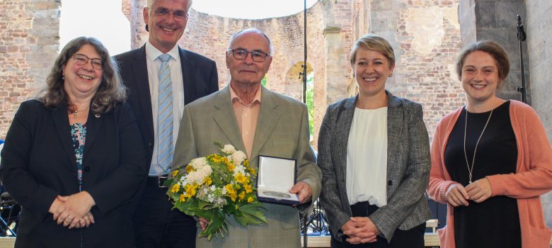 Fünf Personen stehen auf einer Bühne in der Stiftsruine in Bad Hersfeld. Darunter sind Landrat Torsten Warnecke und die Landtagsabgeordneten Tanja Hartdegen, Lena Arnold und Karina Fissmann. Ein Mann hält eine Ehrenplakette und einen Blumenstrauß.