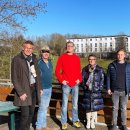 Fünf Personen - Erster Kreisbeigeordneter Dirk Noll, Betreuer Markus Schönhoff, Martin Brosche (Geschäftsführer der Pädagogisch-Therapeutischen Wohngruppen Schumann-Held gGmbH), Jugendamtsleiterin Anette Kranz und Julian Gilbert (Stabstellenleitung im Fachbereich Jugend, Soziales und Senioren) - stehen auf einem Holzbalkon. Im Hintergrund ist eine Wiese mit Bäumen und ein Gebäude zu erkennen.