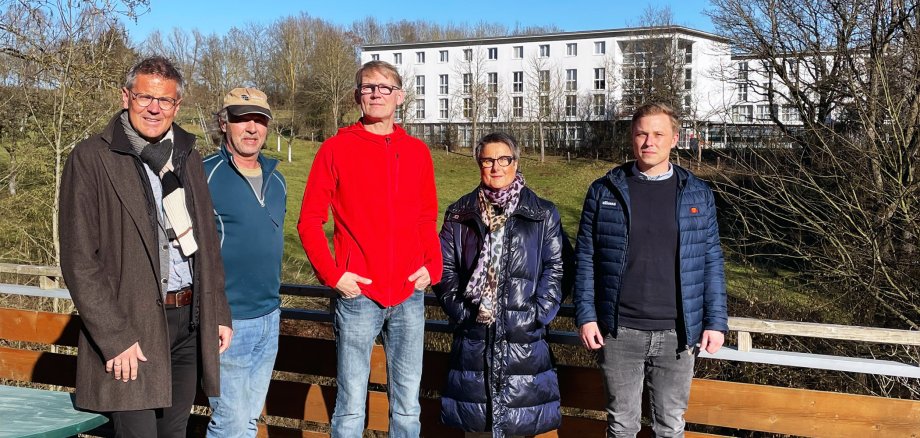 Fünf Personen - Erster Kreisbeigeordneter Dirk Noll, Betreuer Markus Schönhoff, Martin Brosche (Geschäftsführer der Pädagogisch-Therapeutischen Wohngruppen Schumann-Held gGmbH), Jugendamtsleiterin Anette Kranz und Julian Gilbert (Stabstellenleitung im Fachbereich Jugend, Soziales und Senioren) - stehen auf einem Holzbalkon. Im Hintergrund ist eine Wiese mit Bäumen und ein Gebäude zu erkennen.