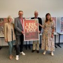 Vier Personen darunter Landrat Torsten Warnecke stehen in einer Reihe in der Modellschule Obersberg. Gemeinsam halten sie ein Poster, das Teil der Ausstellung "Leseland DDR" ist. Im Hintergrund sieht man weitere Teile der Ausstellung, die in der Modellschule Obersberg eröffnet wurde.