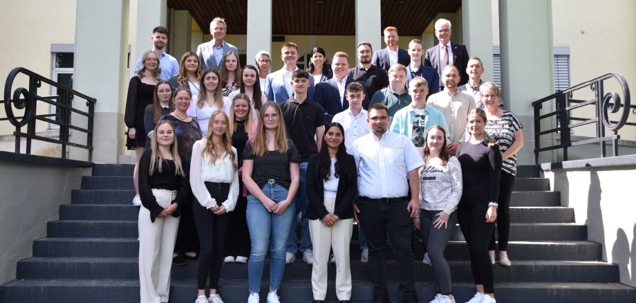 Viele Menschen stehen auf einer Treppe vor dem Landratsamt in Bad Hersfeld. Darunter sind neue Auszubildende, Studierende und Anwärterinnen sowie der Landrat und Erster Kreisbeigeordneter.