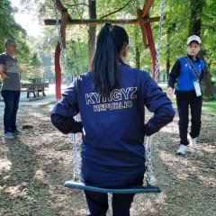 Eine kirgisische Athletin sitzt auf einer Schaukel. Man kann den Aufdruck ihrer Jacke lesen. Dort steht "kirgisische Republik".