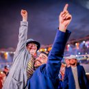 Zwei Personen, eine davon mit Down-Syndrom, stehen in einem großen Stadion und freuen sich. Im Hintergrund sind weitere Personen. Sie alle tragen ähnliche Kleidung. Es ist Nacht.