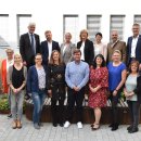 Ungefähr 15 Menschen stehen im Innenhof der Kreisverwaltung. Sie bilden eine Gruppe. Alle schauen glücklich. Drumherum sieht man Pflanzen und im Hintergrund Fenster der Büros.