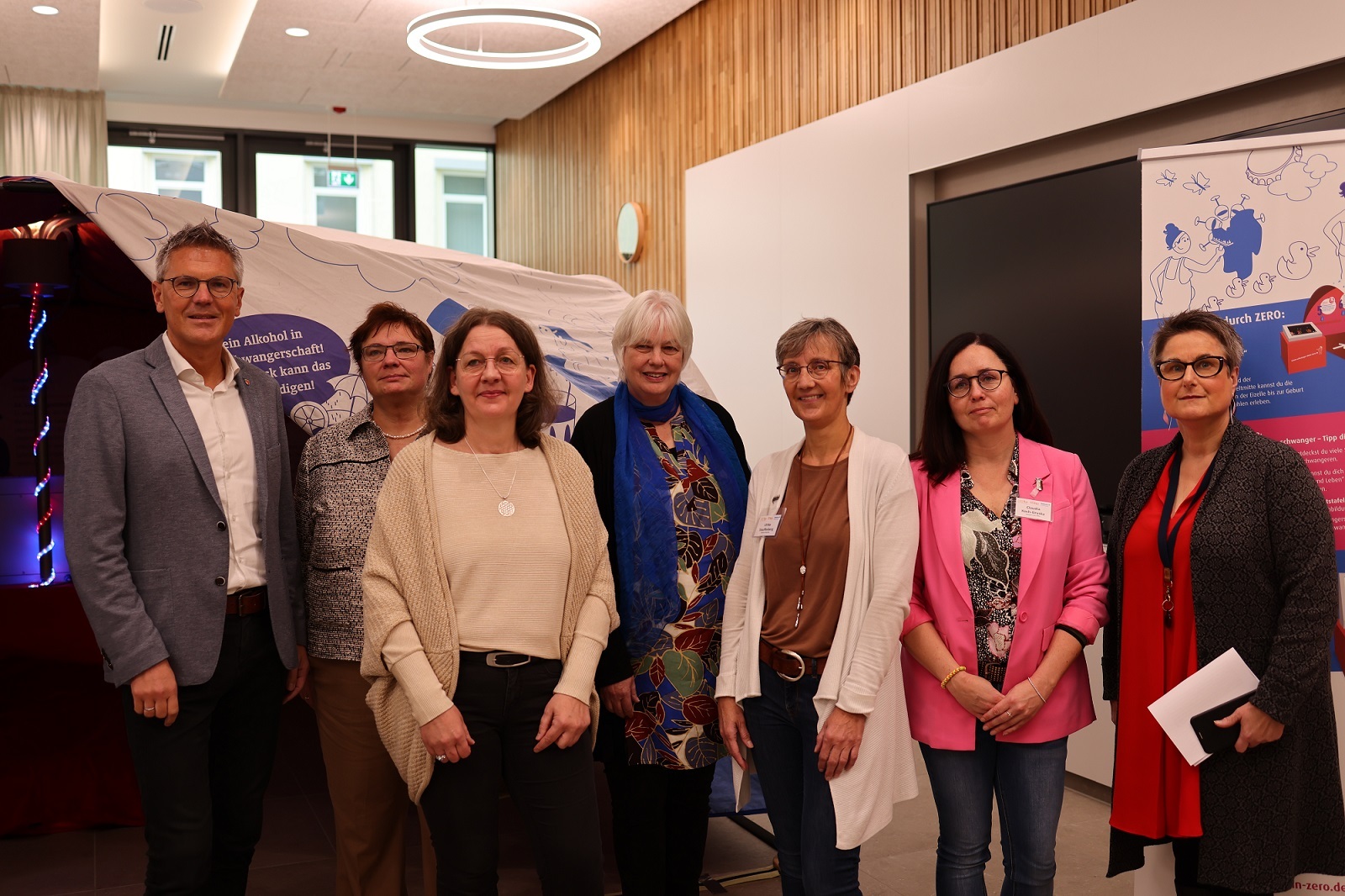 Sieben Personen, darunter ein Mann, stehen im Kreistagssitzungssaal vor einer Teil der Ausstellung zum Thema FASD.
