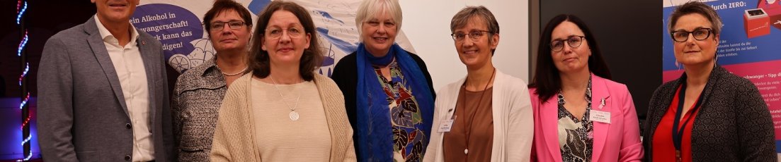 Sieben Personen, darunter ein Mann, stehen im Kreistagssitzungssaal vor einer Teil der Ausstellung zum Thema FASD.