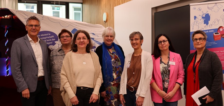 Sieben Personen, darunter ein Mann, stehen im Kreistagssitzungssaal vor einer Teil der Ausstellung zum Thema FASD.