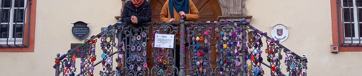Zwei Frauen stehen auf den Treppen des Rotenburger Rathauses. Das Geländer ist mit vielen bunten, gehäkelten Blumen verziert.
