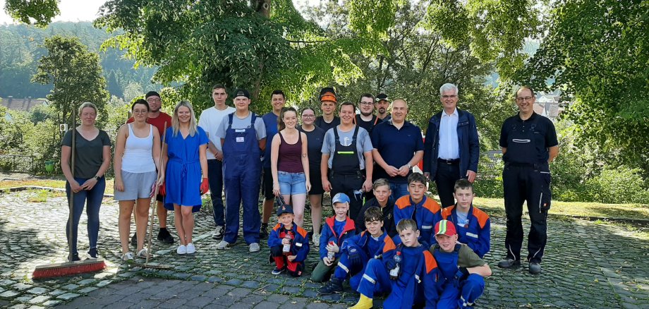 Landrat Torsten Warnecke steht mit freiwilligen Helferinnen und Helfern auf einer grünen Wiese. Im Hintergrund steht ein großer Baum. Es ist sonnig und die Leute freuen sich alle.
