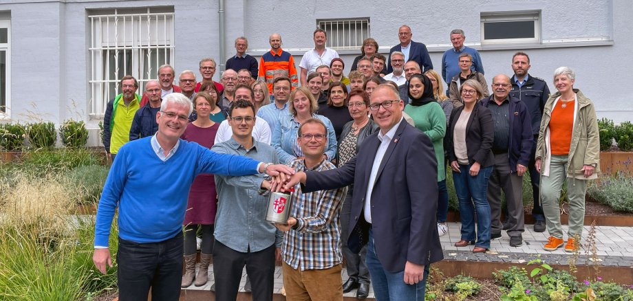 Gruppenfoto auf einer Treppe. Vorne die vier Personen drücken symbolisch auf einen Buzzer mit dem Wappen des Landkreises Hersfeld-Rotenburg darauf. Im Hintergrund stehen rund 40 Personen aufgereiht vor einer grauen Gebäudewand. 