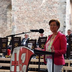 Bad Hersfelds Bürgermeisterin Anke Hofmann steht in der Stiftsruine und spricht ein Grußwort. Sie steht am Pult, an dem das Landkreis-Wappen befestigt ist.