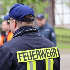 Ein Feuerwehrmann mit reflektierender Schutzkleidung und der Aufschrift „FEUERWEHR“ auf dem Rücken.