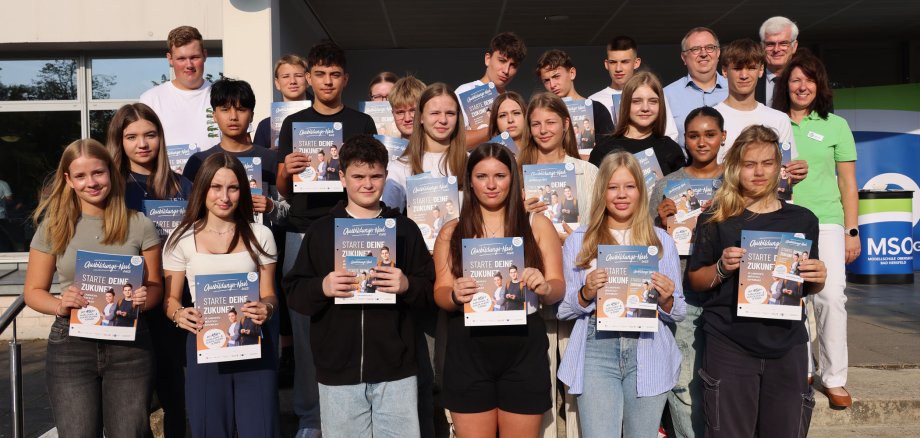 Viele Schülerinnen und Schüler und wenige Erwachsene stehen auf einer Treppe auf dem Schulhof vor der Modellschule Obersberg.