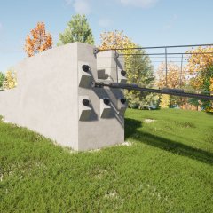 Eine Betonstützmauer mit großen, herausstehenden Bolzen auf einer grünen Wiese. Über die Mauer verläuft eine Brücke mit einem Metallgeländer und Bäume mit herbstlich gefärbten Blättern im Hintergrund.