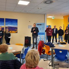 Erster Kreisbeigeordneter Dirk Noll hält ein Mikrofon in der Hand und hält ein kurzes Grußwort an die Anwesenden des Safer-Internet-Day. Im Publikum sitzen viele Seniorinnen und Senioren.