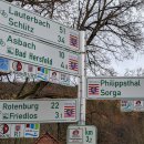 Ein Fahrradwegweiser im Landkreis Hersfeld-Rotenburg. Er zeigt an, wie weit die Distanz zu verschiedenen Orten im Landkreis ist. Im Hintergrund ist ein Baum ohne Blätter zu sehen. Es ist Winter.