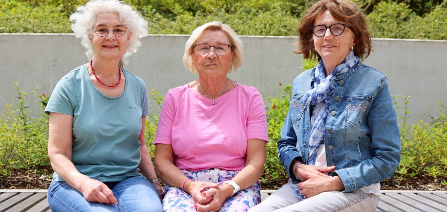 Drei Ehrenamtliche Frauen des Projekts „Hand in Hand“ – Birgit Hillert, Renate Lissek und Helga Hildebrand – sitzen nebeneinander auf einer Bank im Freien. Sie lächeln in die Kamera.