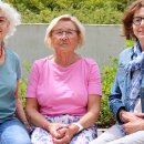 Drei Ehrenamtliche Frauen des Projekts „Hand in Hand“ – Birgit Hillert, Renate Lissek und Helga Hildebrand – sitzen nebeneinander auf einer Bank im Freien. Sie lächeln in die Kamera.