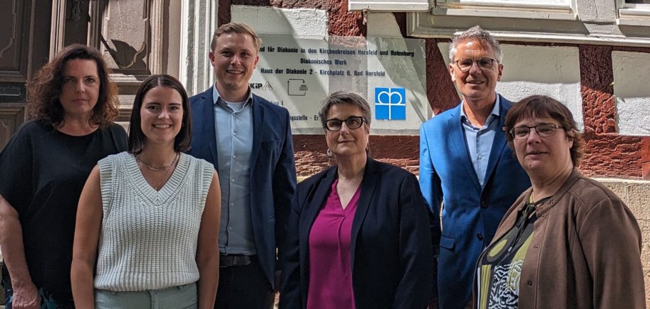 Zwei Männer und vier Frauen stehen vor einem Fachwerkhaus. Im Hintergrund sieht man ein Schild, auf dem die Adresse der Diakonie steht. Die Personen lächeln in die Kamera.