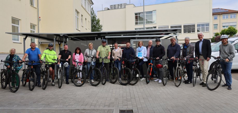 Mitarbeitende der Kreisverwaltung und Landrat Torsten Warnecke stehen vor der neuen Fahrradabstellanlage am Landratsamt. Jeweils neben ihnen stehen ihre Fahrräder. Sie freuen sich.
