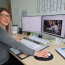 Eine Frau sitzt an ihrem Arbeitsplatz an einem Schreibtisch und hat auf dem Computer ein Video zur Hygieneschutzbelehrung laufen.