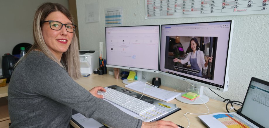 Eine Frau sitzt an ihrem Arbeitsplatz an einem Schreibtisch und hat auf dem Computer ein Video zur Hygieneschutzbelehrung laufen.