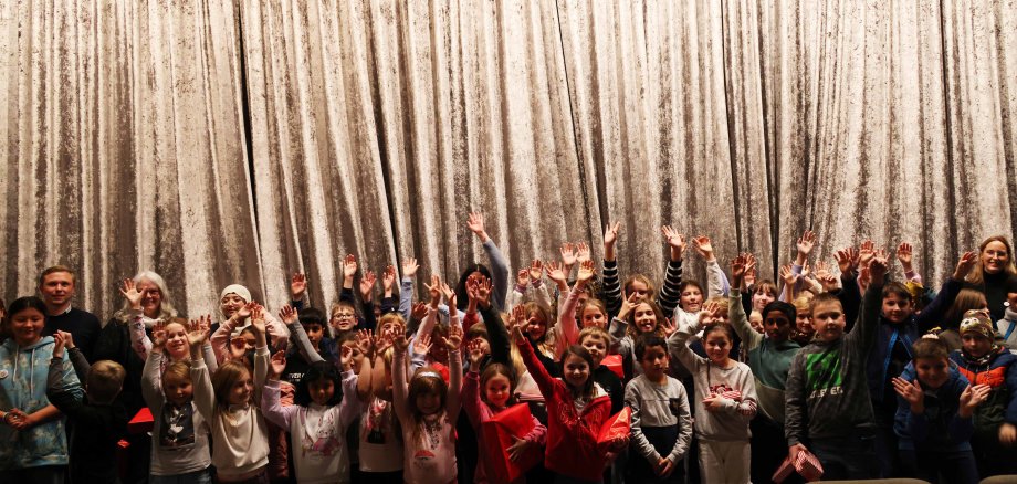 Viele Kinder stehen vor dem Vorhang in einem Kino-Saal