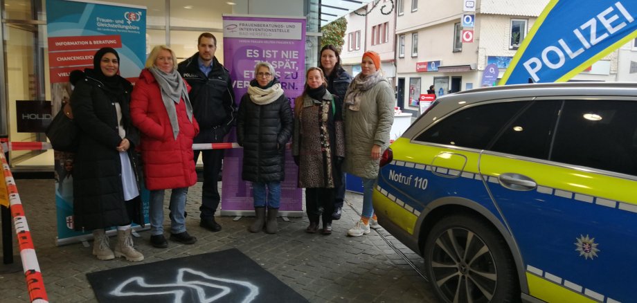Einige Menschen stehen an der abgesperrten Tatort-Nachbildung. Auf der rechten Seite sieht man ein Polizei-Auto. 