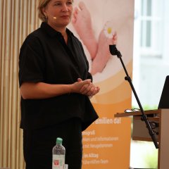 Eine blonde Frau steht im Kreistagssitzungssaal des Landkreises und trägt ein Mikrofon. Sie redet zu den Leuten im Saal.